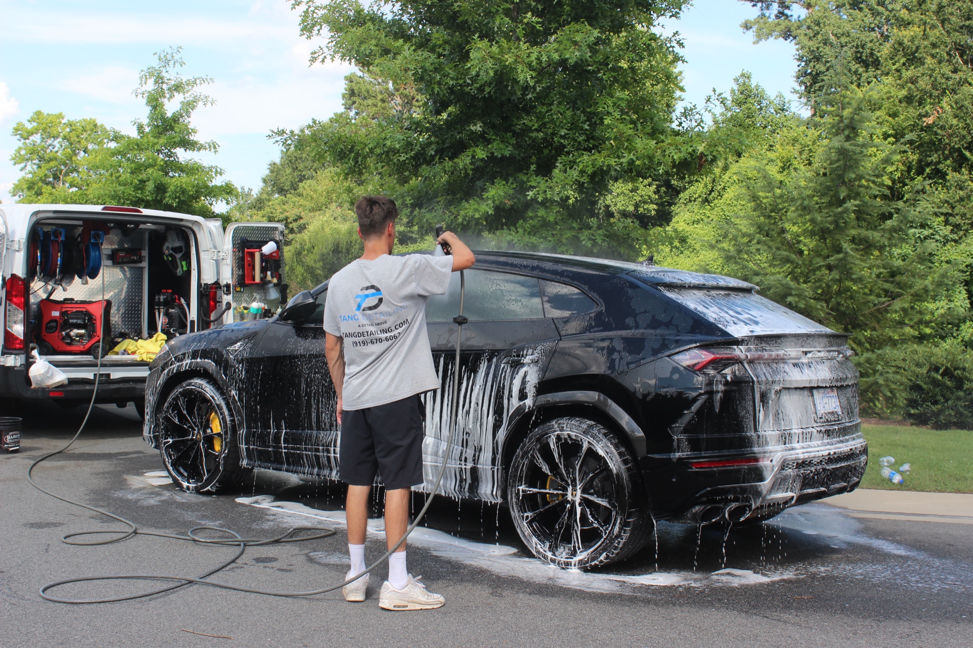Tang Detailing technician foam hand washing the black 2024 Lamborghini Urus beside the mobile detailing van in Raleigh NC