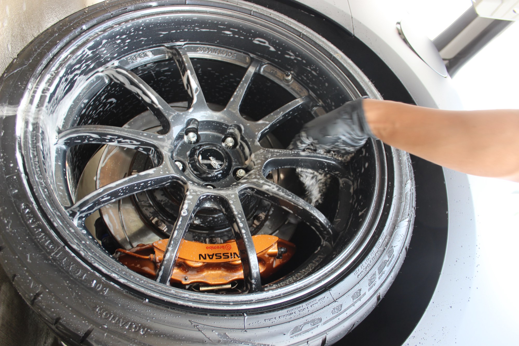 Tang Detailing hand washing a wheel and orange Nissan GT-R brake caliper during a full detail in Raleigh NC